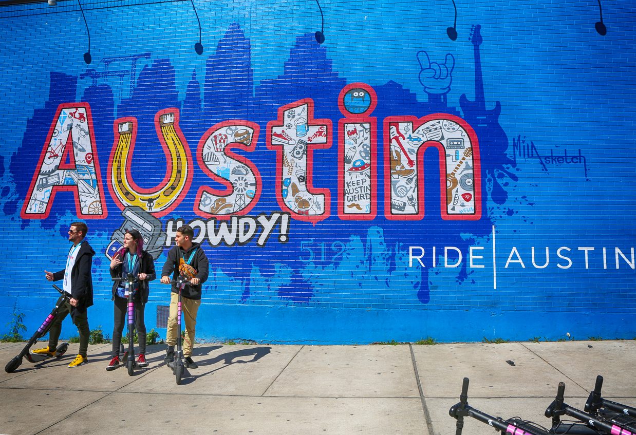Members of SXSW in front of wall painting at 6th Street, Austin, using electric scooter-popular transportation in city