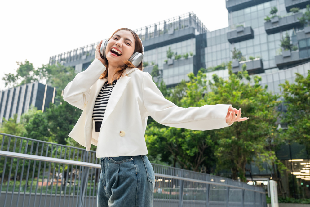 Young Asian woman fashion lifestyle with headphone standing posing dancing in urban city downtown. Happy attractive charming Asian female listen to the music and dance. People and lifestyle
