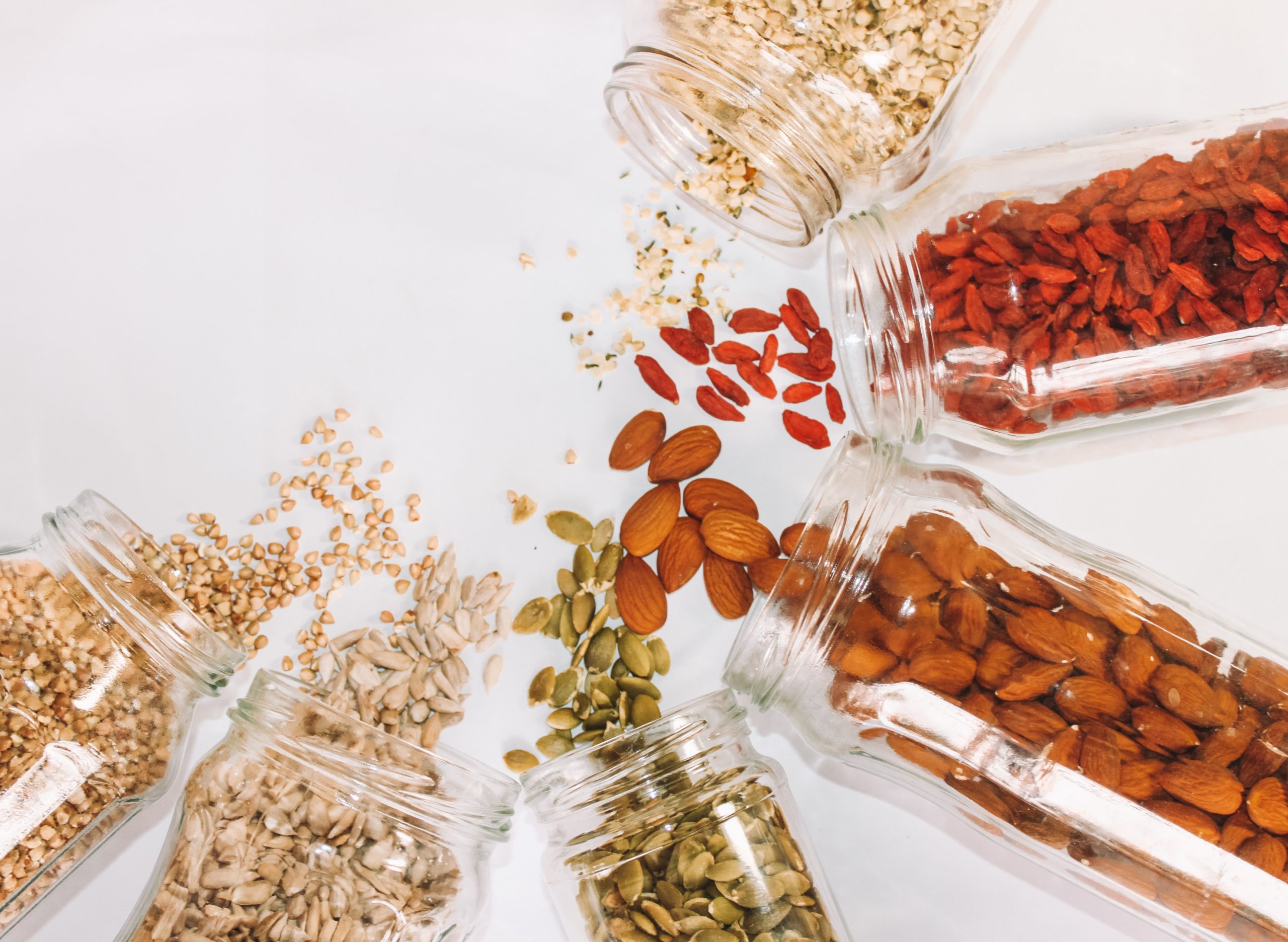 Jars of a variety of nuts and seeds spilled on a white table
