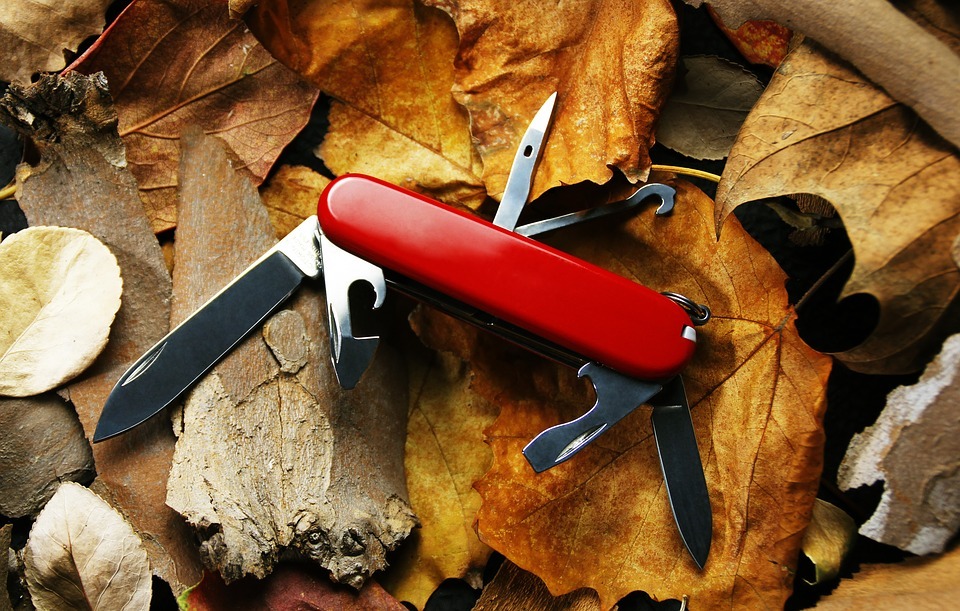 An open Swiss army knife on top of a pile of wood and leaves
