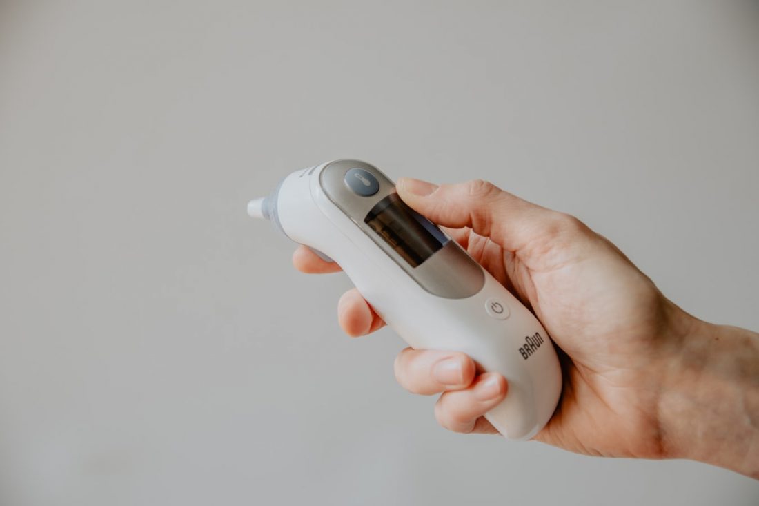 person holding a forehead and ear thermometer