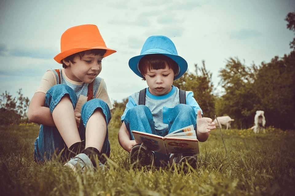 two kids sitting on the grass, reading a book