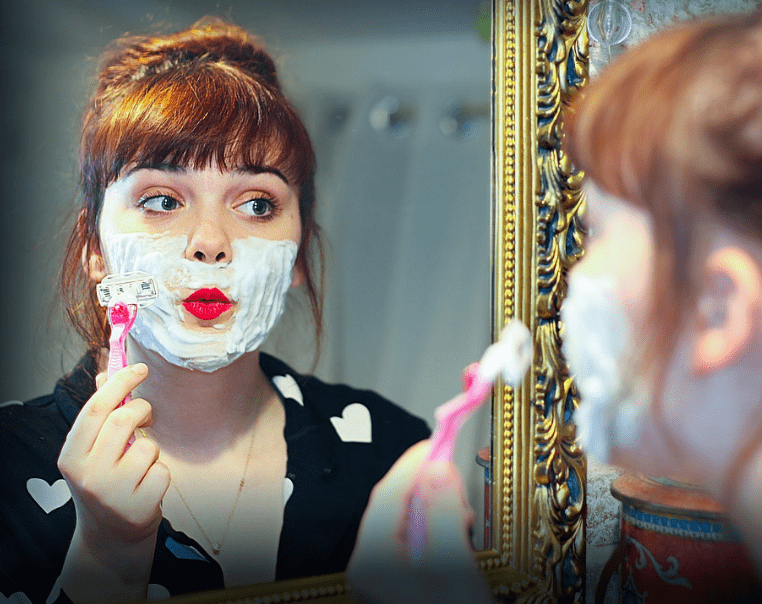 A woman with shaving foam and razor.