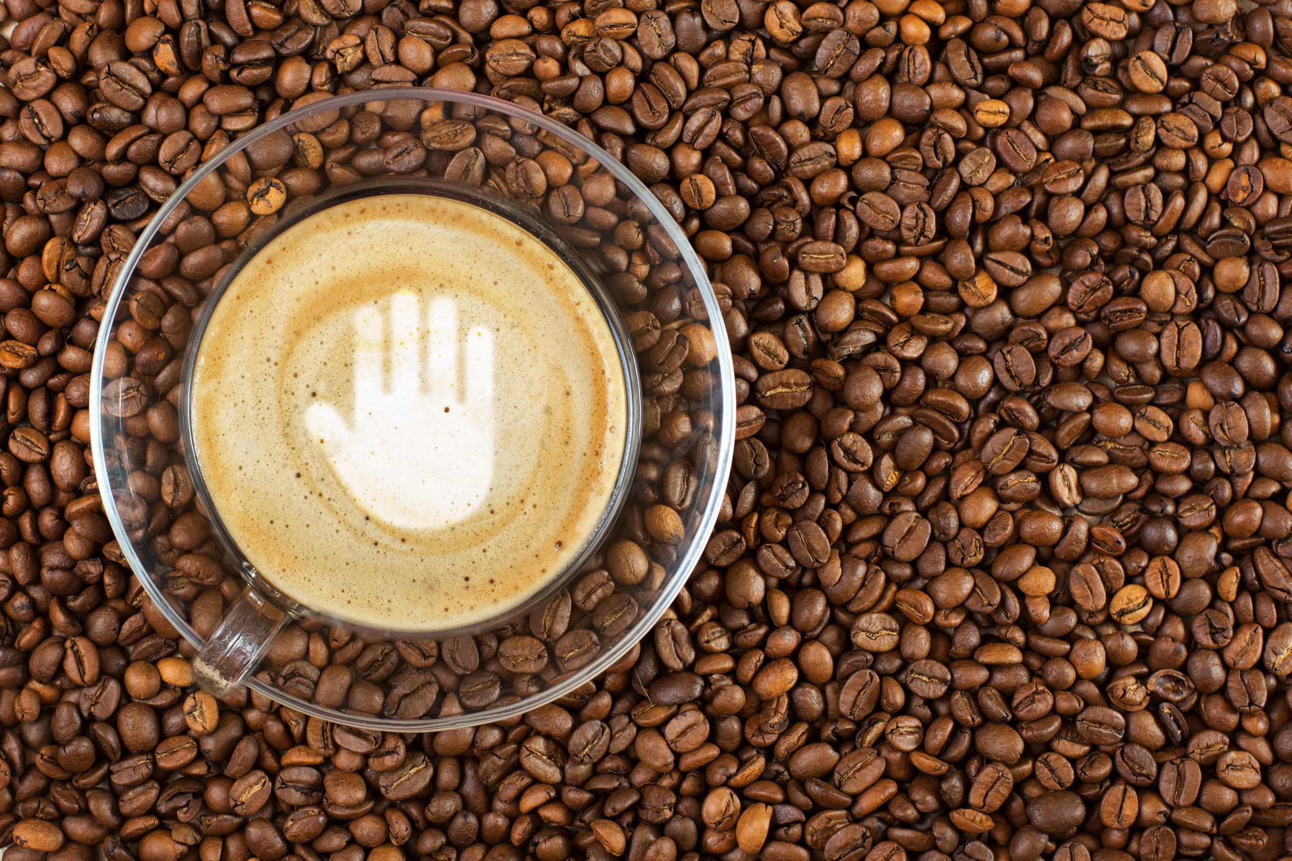 Cup of espresso with stop gesture sign on coffee foam on coffee beans background. With copy space