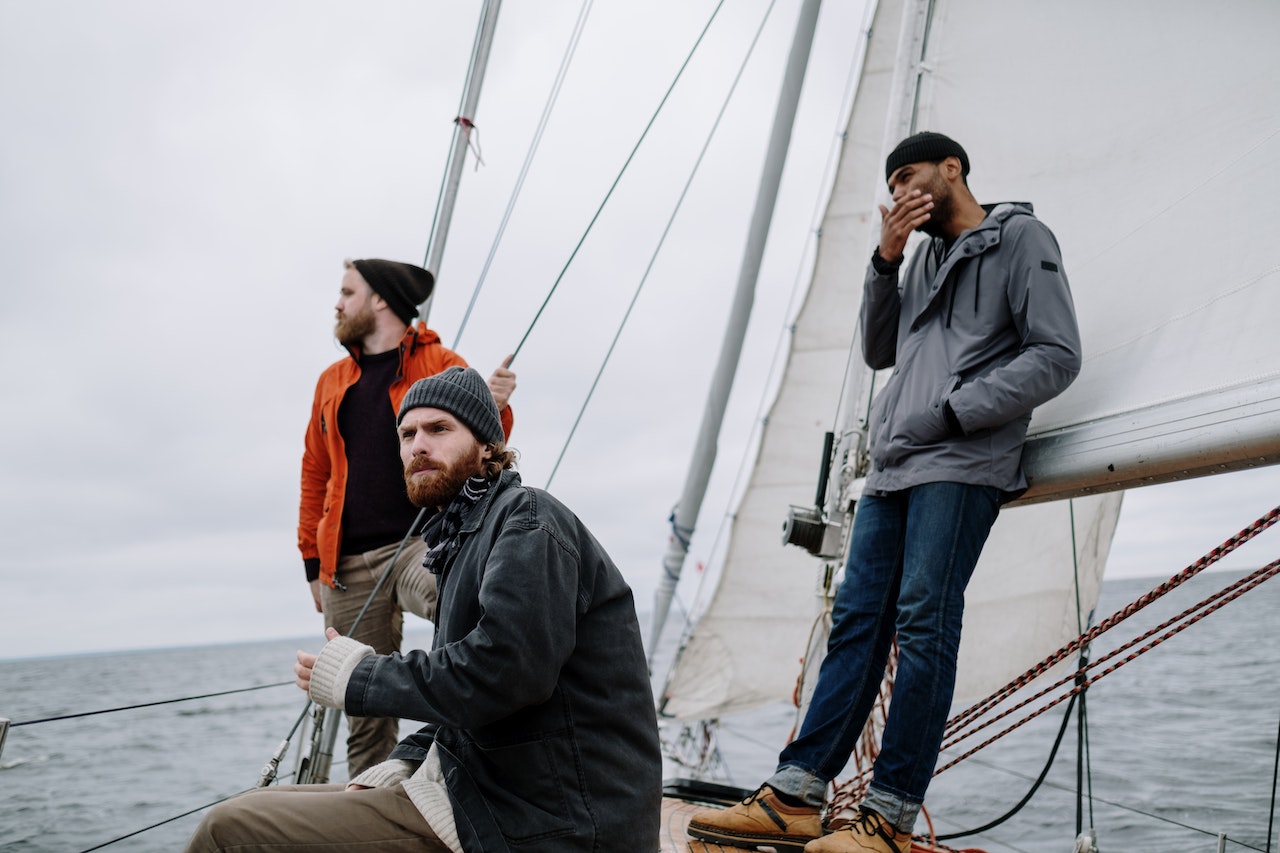 three men on a sailboat wearing windbreakers
