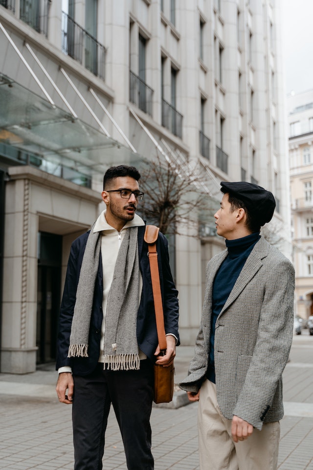 two men in blazers talking beside a tall building